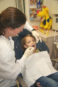 Pediatric dentist examining young child's teeth in dental office treatment room.