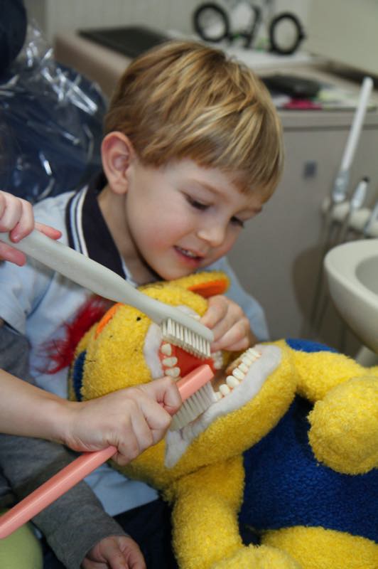 Young child holding yellow stuffed animal in dental office setting.
