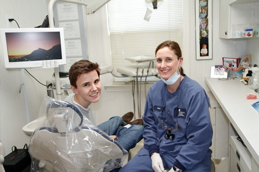 Two dental professionals in clinical attire working together in a modern dental office treatment room.