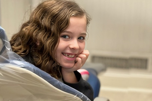 Young girl smiling at camera in dental office setting wearing blue bib.