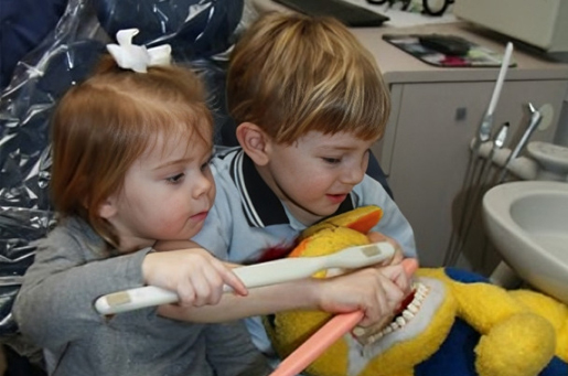 Two young children holding a yellow snake during a dental office visit.
