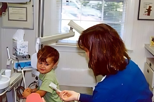 Young child receiving dental examination from female dentist in blue scrubs at dental office.