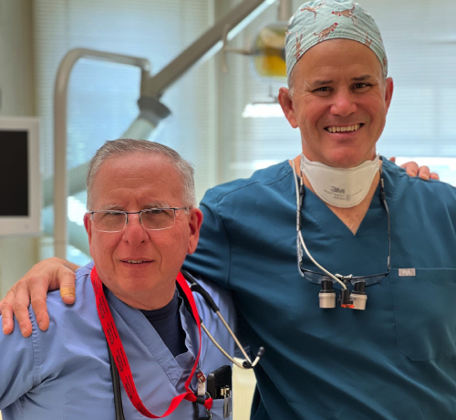 Two dental professionals pose together in a clinical setting, wearing scrubs and stethoscopes.