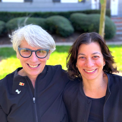 Two women smiling outdoors in front of Ferguson Dental office building and landscaping.