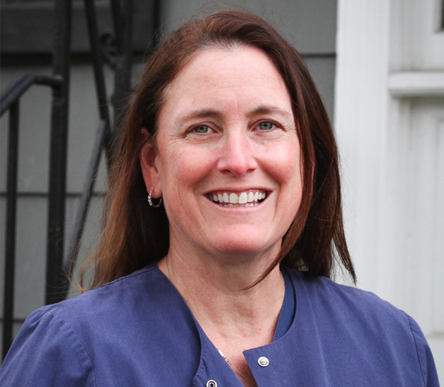 Woman in blue scrubs smiling at camera, dental office professional portrait.