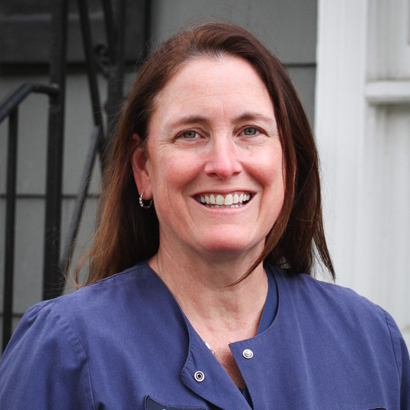 Smiling woman in blue scrubs at Ferguson Dental practice, professional headshot outdoors.