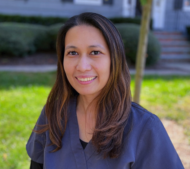 Professional headshot of female dental staff member smiling outdoors against green lawn background.