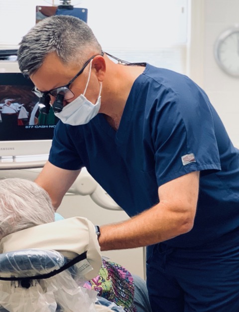 Dentist in blue scrubs and mask examining patient in dental office setting.