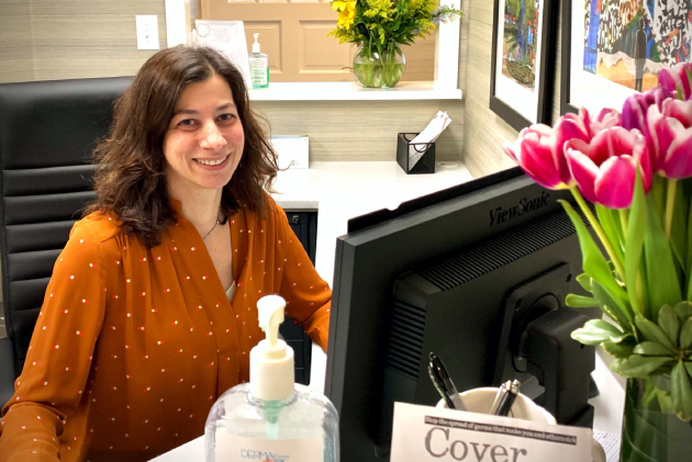 Woman smiling at desk in dental office with computer and flowers visible.