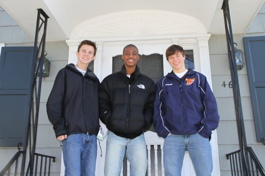 Three men standing inside a white van or vehicle, wearing casual jackets and jeans.