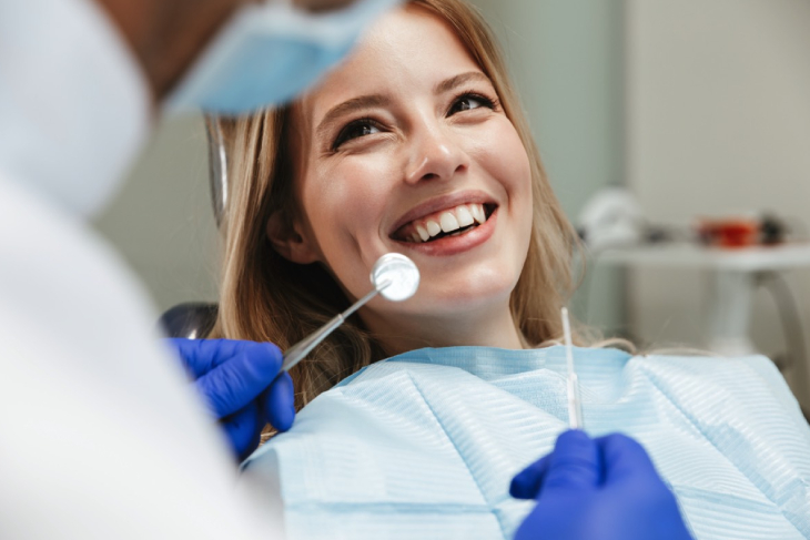 Young woman smiling in dental chair during examination with dentist holding tools.