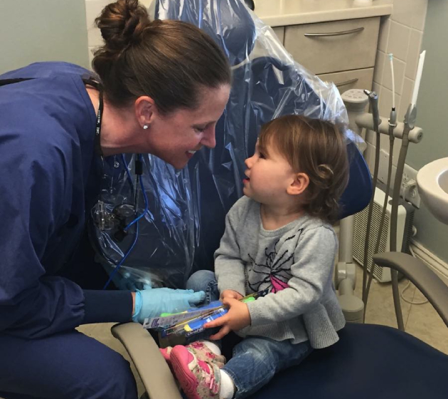 Pediatric dentist examining young child's teeth in dental office treatment room.