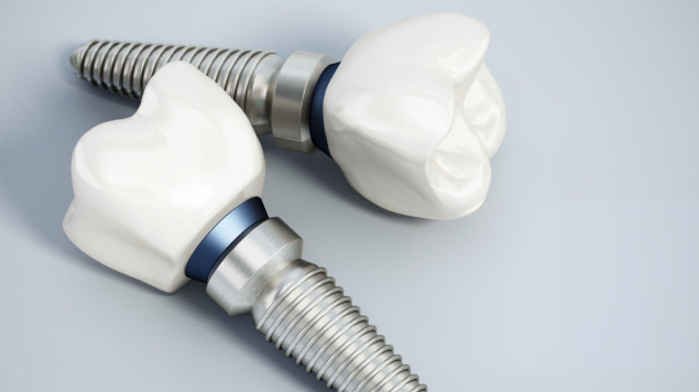 Two dental implant abutments with white ceramic crowns attached to metal screws on gray surface.