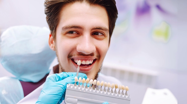 Smiling dentist holding dental model showing teeth alignment in clinical office setting.