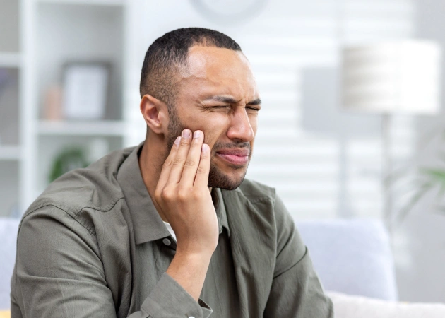 Man experiencing tooth pain, holding cheek, in bright office setting.