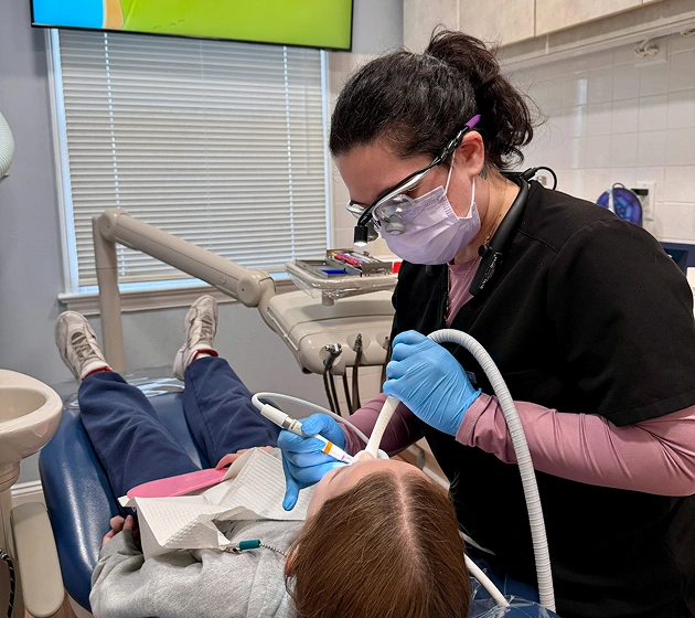 Dentist in protective gear examining young patient in dental chair at Ferguson Dental office.