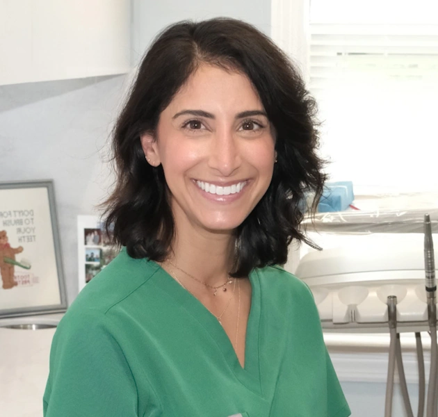 Woman in green scrubs smiling at camera in dental office setting.