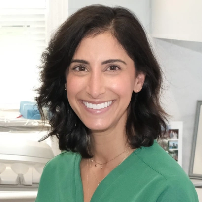 Woman in green dental scrubs smiling at camera in dental office setting.