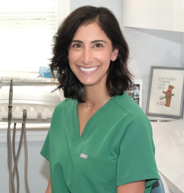 Smiling dental professional in green scrubs at Ferguson Dental clinic workspace.